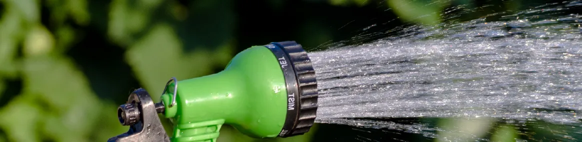 Garden hose with green water-efficient nozzle spraying water on blurred landscape in background
